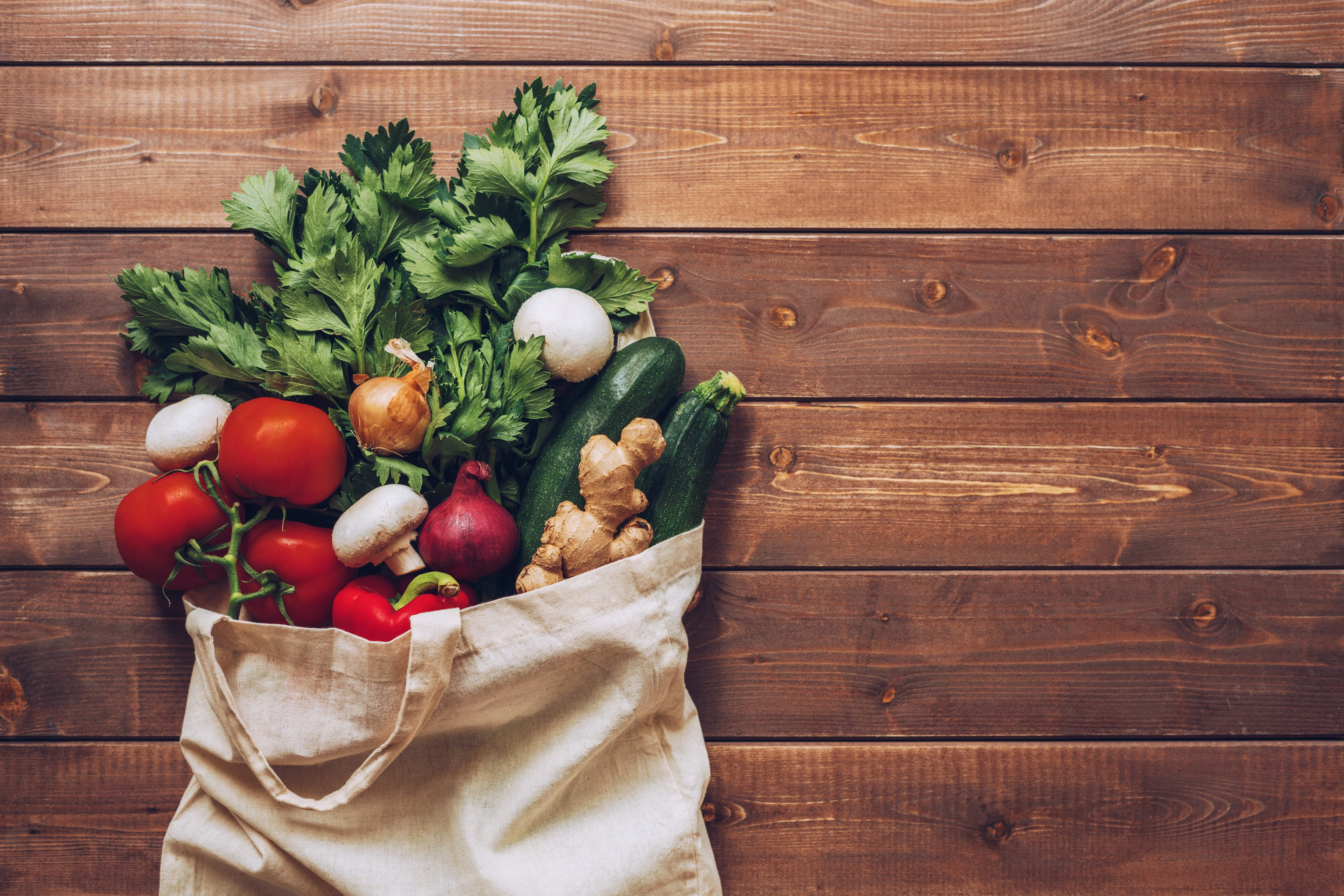 A bag of fresh, organic vegetables spilling onto a rustic wooden countertop, highlighting natural, wholesome produce and farm-to-table freshness.